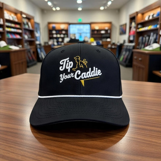 Black cap with embroidered OG 'Tip Your Caddie' logo on a wooden table in a golf pro shop